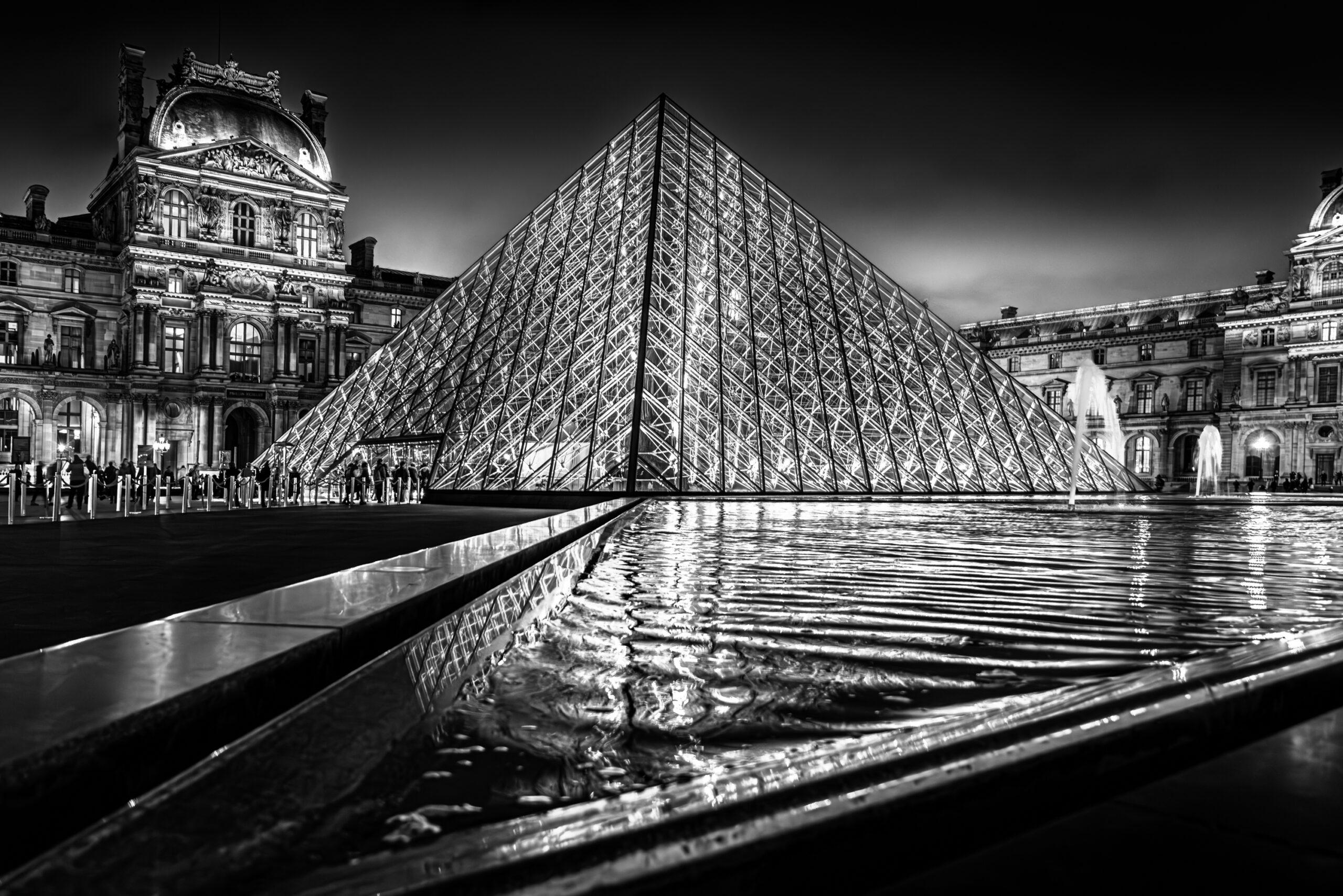 A black and white fine art photograph of the Louvre Pyramid at night, capturing geometric symmetry, architectural contrast, and timeless elegance in Paris.